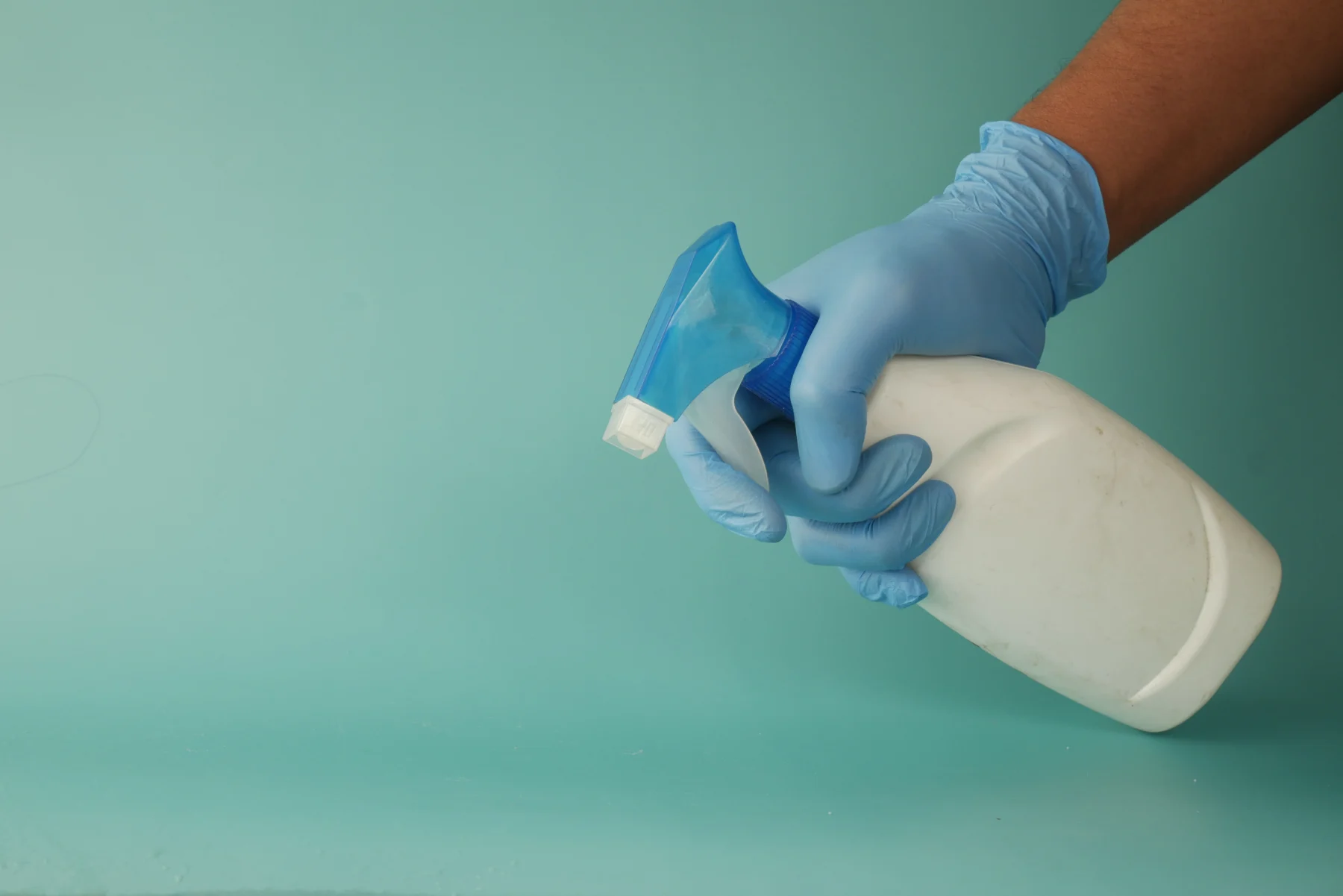 Tangan bersarung tangan menyemprotkan disinfektan ke permukaan meja