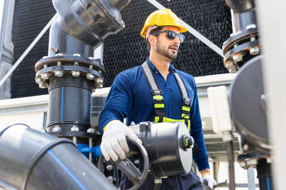 Teknisi berhelm dan harness memeriksa sistem cooling tower industri